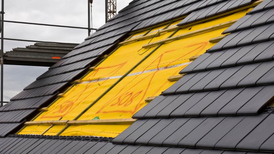 Toit en construction avec des tuiles en cours de pose sur une sous-couche jaune.